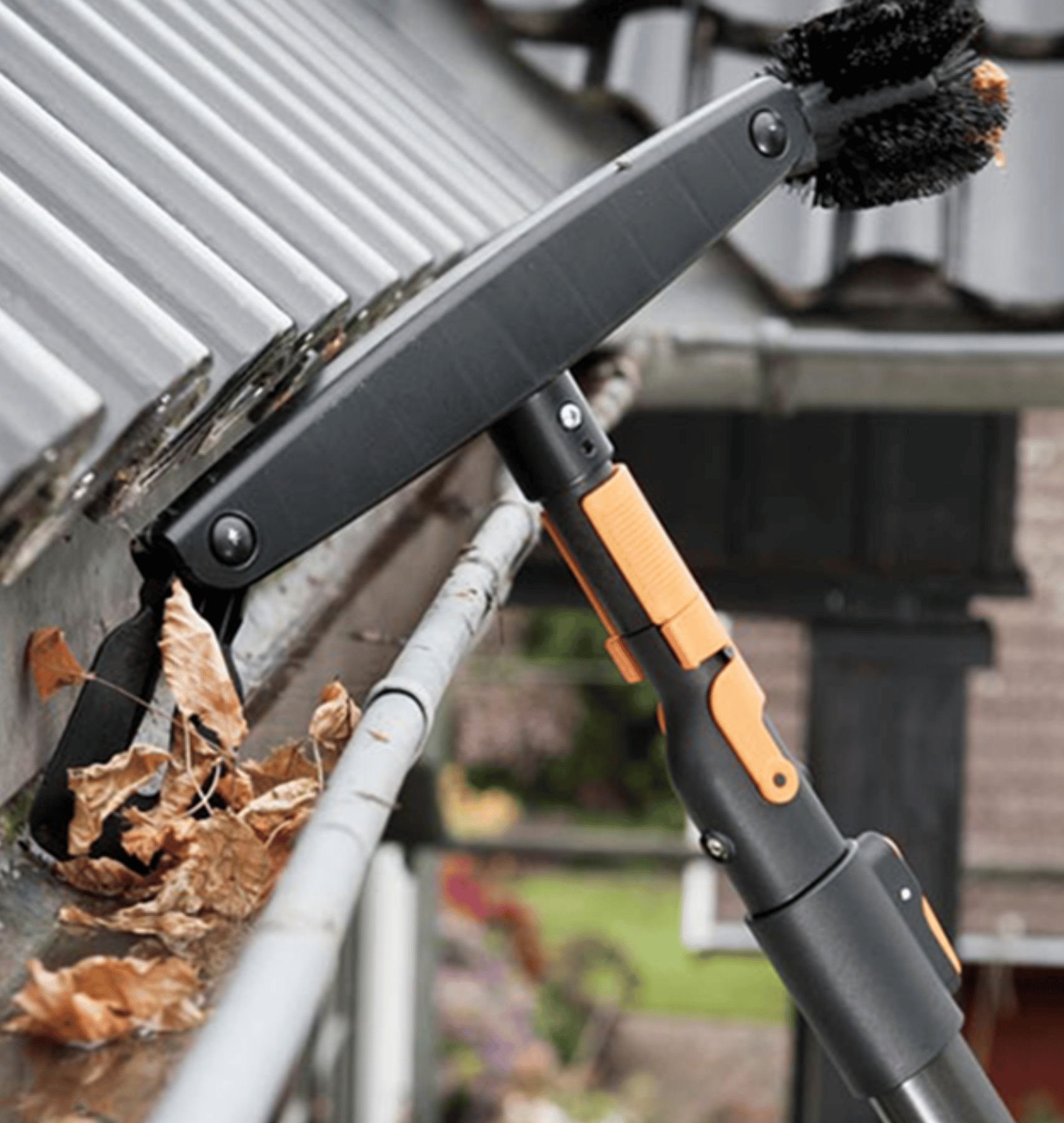 Cleaning apparatus like a squeegee and brush to remove leaves from a gutter full of brown leaves on a roof